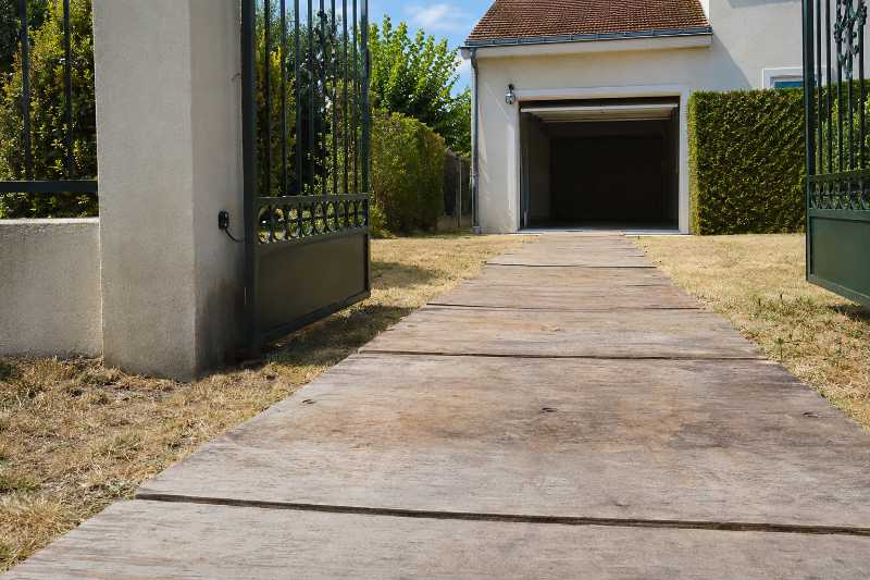 Chemin de roulement en plaques de bois posé sur une pelouse jusqu'à une porte de garage relevée