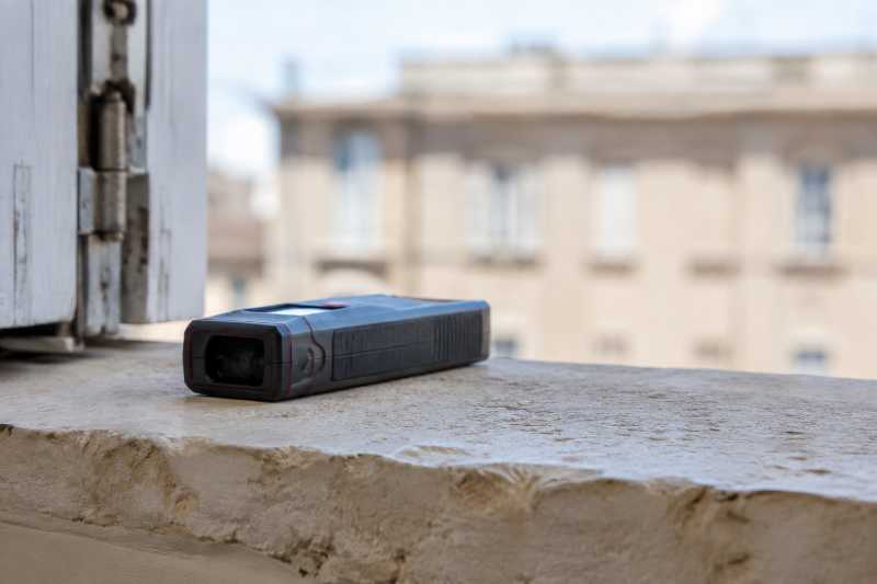 Télémètre laser posé à plat sur un appui de fenêtre en pierre, façade d'en face floutée derrière
