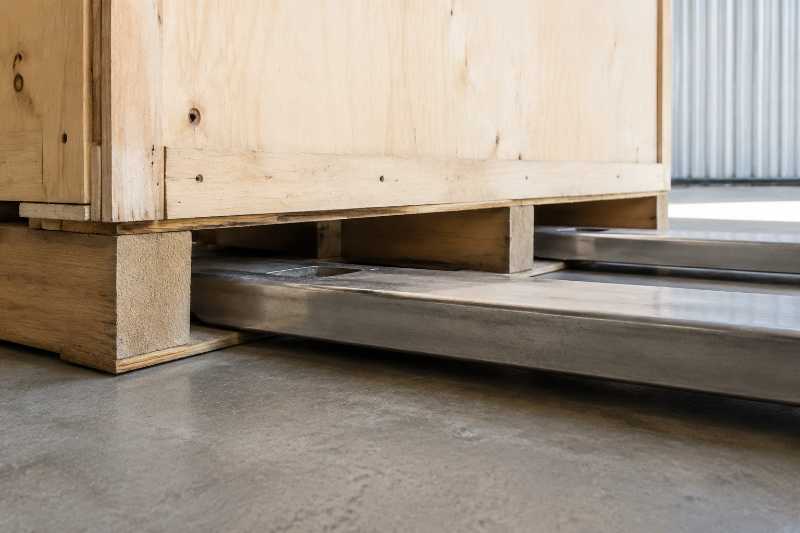 Fourches d'un transpalette engagées sous le patin d'une caisse de garde-meuble, sol béton