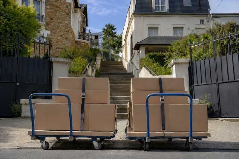 Deux chariots plats chargés de cartons sanglés, au pied d'un escalier extérieur en béton